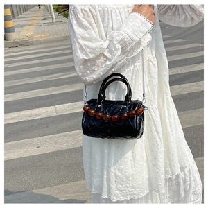 Detalle de bolso Boston negro plisado con cadena plateada y decoración de cuentas ámbar