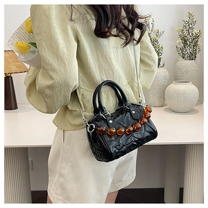 Detalle de bolso Boston negro plisado con cadena plateada y cuentas de ámbar decorativas