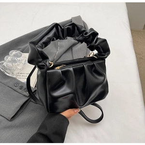 Close-up of black ruched leather handbag with gold zipper on grey blazer backdrop