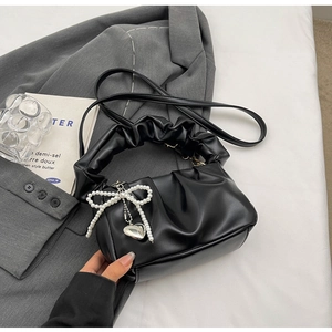 Detailed view of black pleated cloud bag with pearl bow and silver heart pendant charms