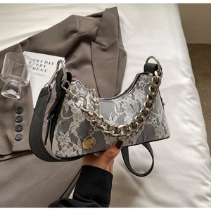 Detailed shot of white floral lace fabric on a grey crossbody bag with silver chain