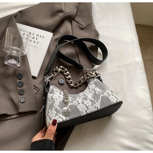 Detail of black leather underarm bag with white lace embroidery and silver chain strap