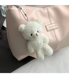 Close-up of white plush bear keychain with metal chain on a pink leather handbag