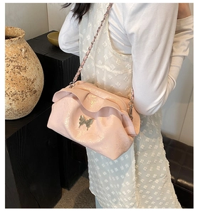Detail of light pink pleated cloud bag featuring golden butterfly ornament and chain strap