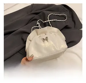 Close-up of white ruched cloud bag featuring a silver butterfly buckle and chain strap
