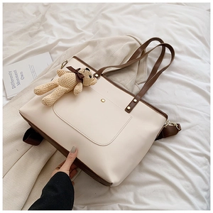 Detail der cremebraunen Shopper-Tasche mit Bärenanhänger auf weißem Bettwäsche-Hintergrund