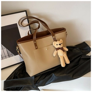 Nahaufnahme der zweifarbigen Tote Bag mit Bärenanhänger auf schwarzem Lederhintergrund