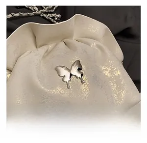 Macro detail of white pleated bag with silver butterfly charm and chain strap