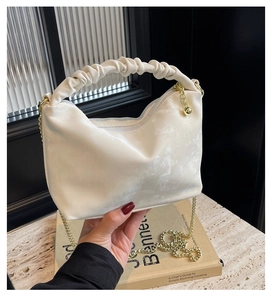 Detail of ruched handle and gold chain strap with ball pendant on beige crossbody bag