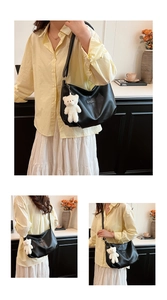 Detail of black leather tote bag with white plush bear charm and minimalist stitching