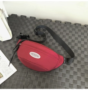 Détail du sac bandoulière bordeaux montrant le nylon, l'écusson et la sangle noire