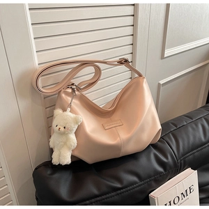 Detail of apricot crescent bag with plush bear charm and adjustable strap on leather sofa