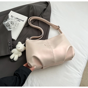 Detail of cream leather tote bag featuring vertical stitching and a plush bear pendant