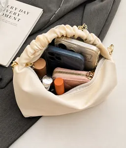 Spacious interior of beige ruched cloud bag with golden chain and makeup items