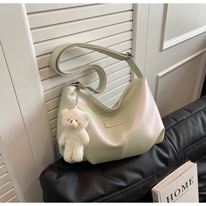 Detail of light green pearl tote bag with teddy bear charm on a leather sofa