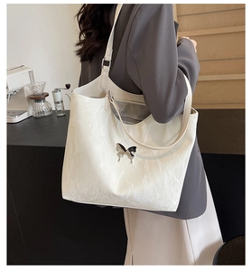 Detail of cream-colored bow tote bag with metallic butterfly and wrinkled PU leather texture