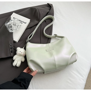 Detail of light green leather tote bag with pleated texture and white teddy bear charm