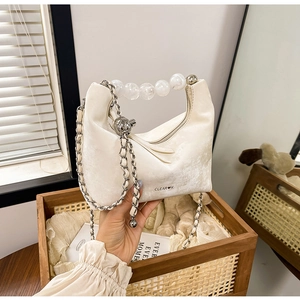 Close-up of velvet off-white handbag with beaded handle and metal chain strap detail