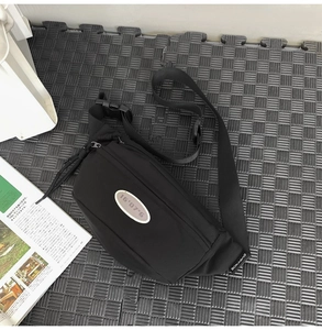 Détail d'un sac bandoulière noir en nylon avec patch logo ovale et sangle réglable