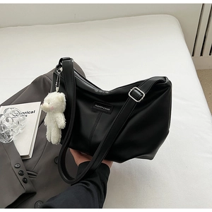 Detail of a large black leather hobo bag featuring a white plush bear charm and fashion label
