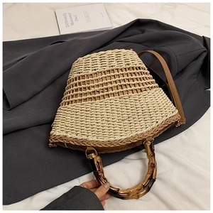 Close-up of woven straw bucket bag with dark bamboo handle and brown leather shoulder strap