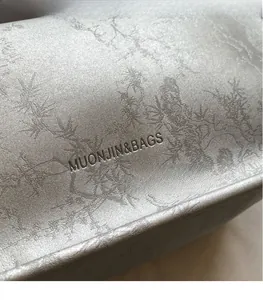 Close-up of metallic silver bag with branch pattern embossing and brand logo detail