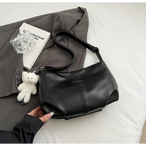 Close-up of black matte leather tote bag with a white plush bear charm and wide strap