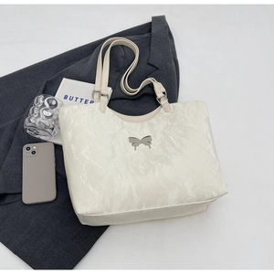 Detail of white wrinkled faux leather tote bag with silver butterfly emblem