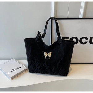 Detail showing textured black tote bag with silver bow charm and V-shaped cut design