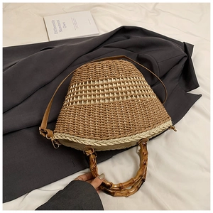Detail of hand-woven straw bucket bag with dark brown bamboo handle and leather strap