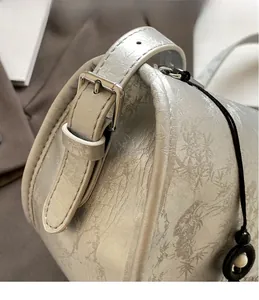 Detail of adjustable metal buckle and embossed texture on stylish underarm bag