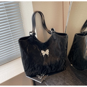 Detailed close-up of a black pleated tote bag featuring a silver butterfly metal ornament