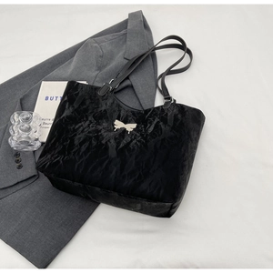 Detail of black glossy pleated tote bag featuring a decorative silver metal bow accent