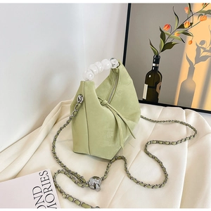 Detail of light green beaded handle handbag with metal chain strap and tassel on fabric