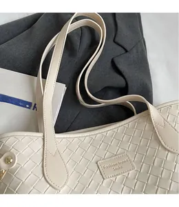 Close-up of beige woven tote bag detailing shoulder strap and leather brand tag