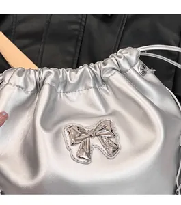 Detail of silver metallic drawstring bucket bag with a decorative metal bow accent