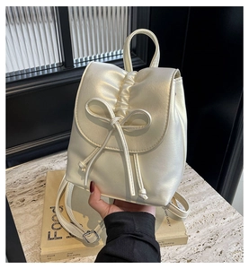 Détail d'un sac à dos plissé crème avec nœud élégant et finitions métalliques argentées