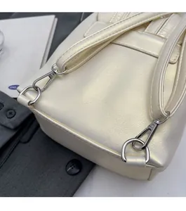 Gros plan sur la texture nacrée et les boucles en métal argenté du sac à dos crème