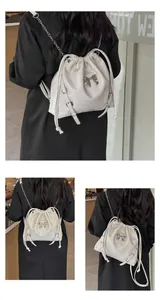 Vertical view of a cream drawstring backpack with chain straps and a silver bow detail