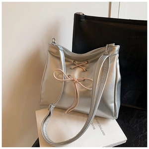 Detail of silver metallic shoulder bag featuring a pink bow on a white book backdrop