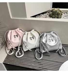 Three drawstring bucket bags in pink, white, and silver with bow details and chain straps