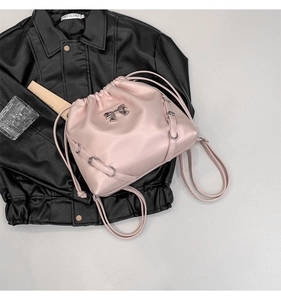 Detail of light pink drawstring backpack with silver bow buckle on black leather backdrop