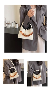 Detail of cream leather handbag with amber bead chain and adjustable crossbody strap