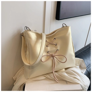 Detailed close-up of cream bow shoulder bag with cross-lace texture and silver hardware