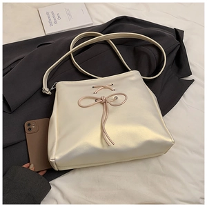 Detail of a creamy beige ballet-style shoulder bag featuring a pink ribbon bow design