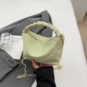Fashionable mint green pleated handbag with gold chain strap held against grey suit