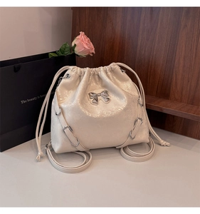 Detail of creamy white drawstring bucket bag with silver bow accent and crinkled patent finish