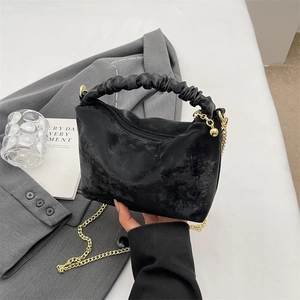 Chic black pleated handbag with vintage texture and gold chain on a neutral background