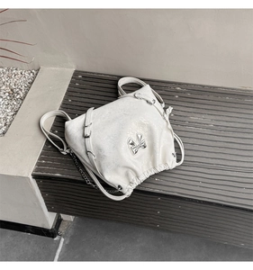 Detail of a beige drawstring backpack featuring a silver bow and metallic chain accents