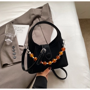 Detail of black half-moon handbag featuring amber bead chain and matte leather texture